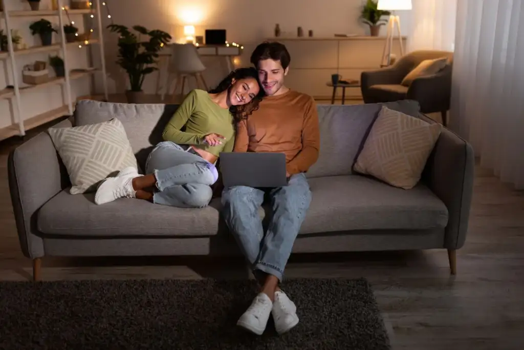 Paar sitzt abends mit Laptop auf dem Sofa und arbeitet den Online-Kurs HerzschrittMACHER durch
